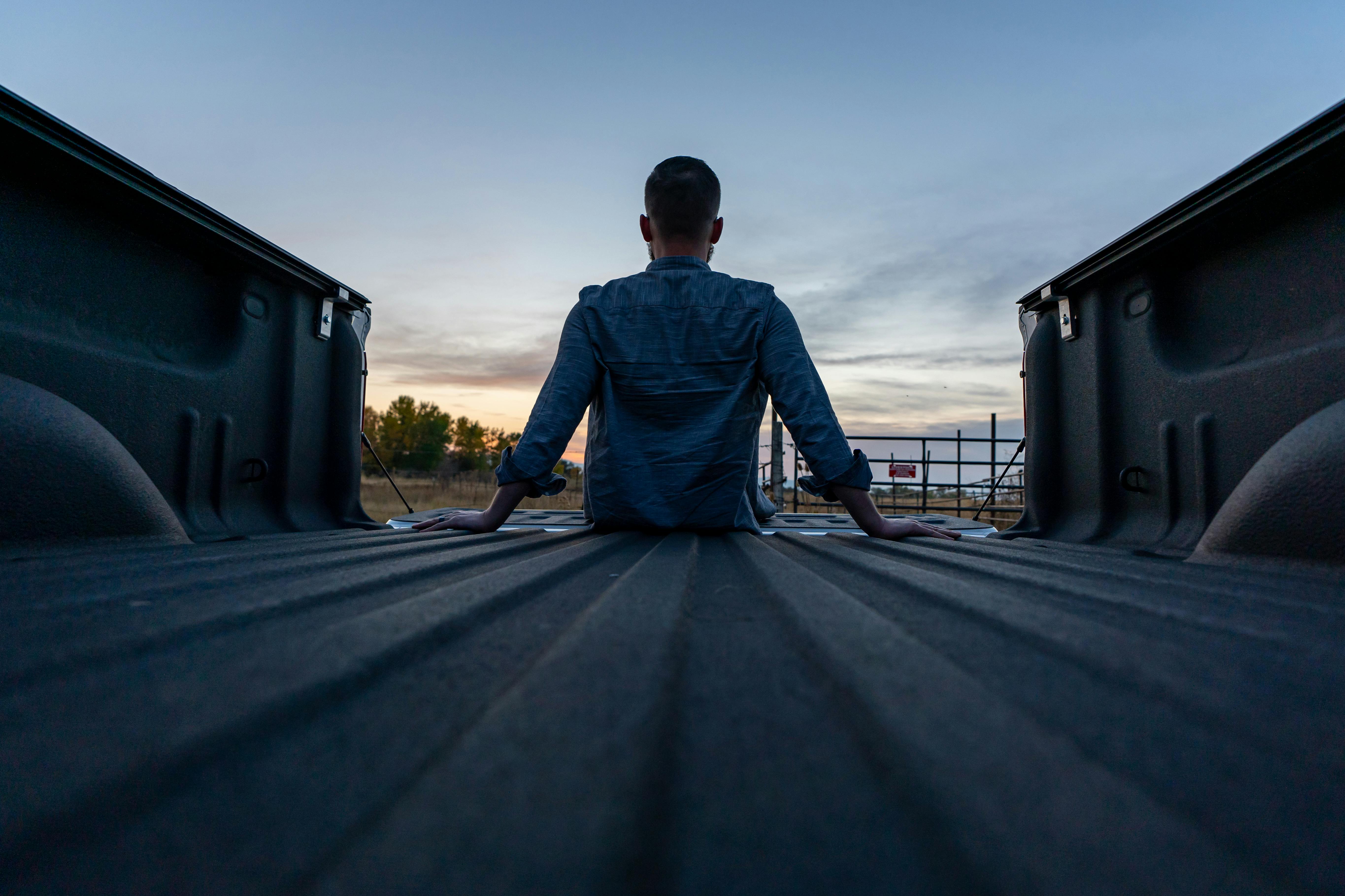 Back of man sitting on edge of truck bed silhouetted against the sunset