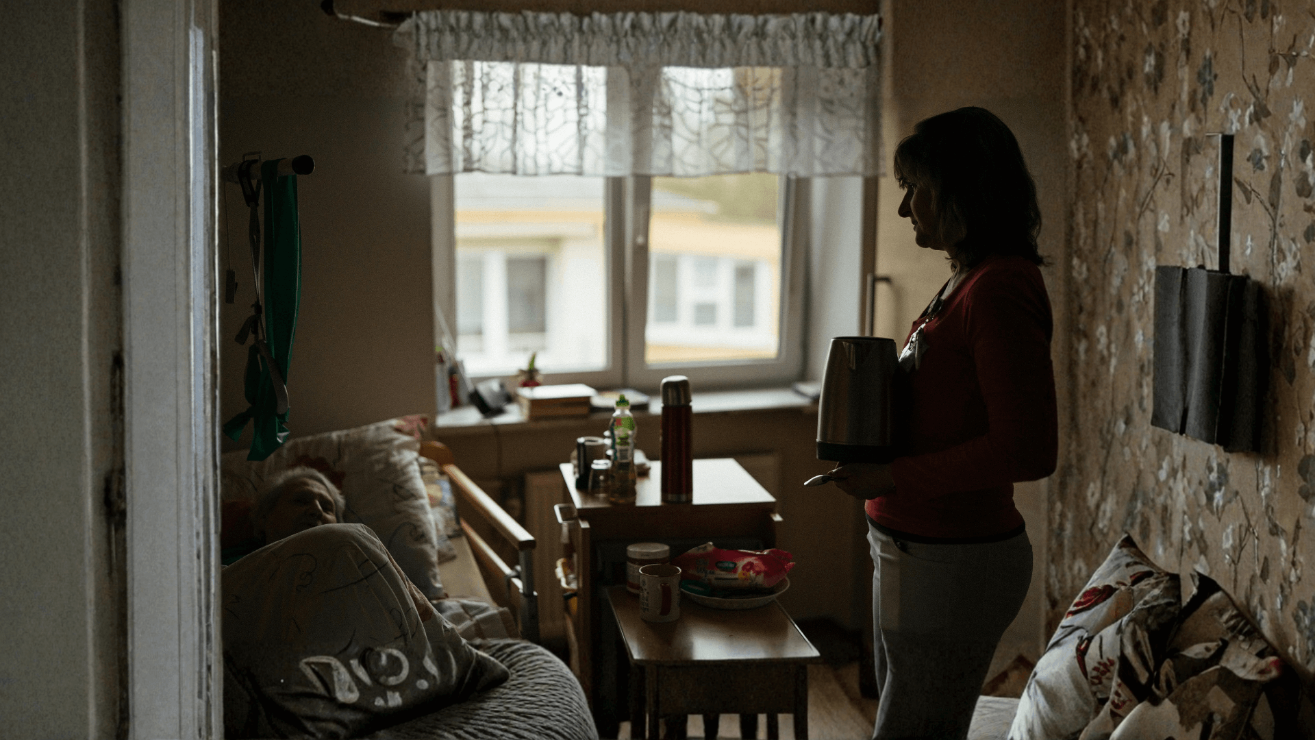 Caregiver stands by hospital bed, offering support.