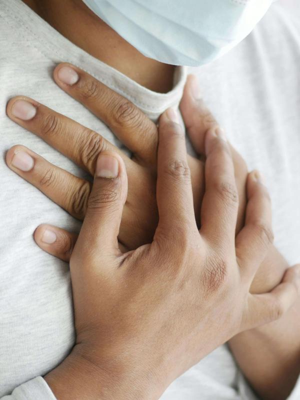 A masked person places both hands over their chest, suggesting a grounding or breath-focused self-regulation practice.