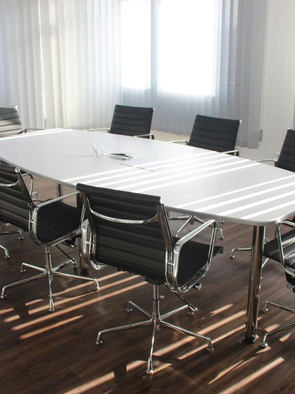 Empty conference room with a large table and office chairs near bright windows, suggesting a quiet, private space that could be used for brief breaks or regrouping during the workday.