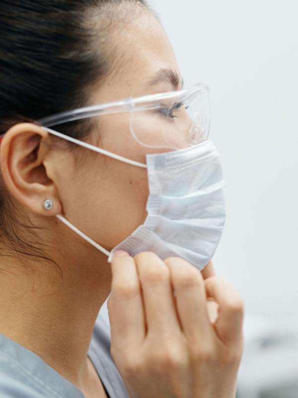 A healthcare professional wearing protective goggles adjusts a surgical mask before patient care in a clinical setting.