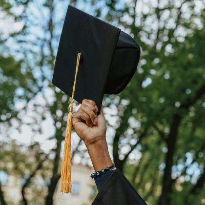 A graduate raises a cap outdoors during commencement.
