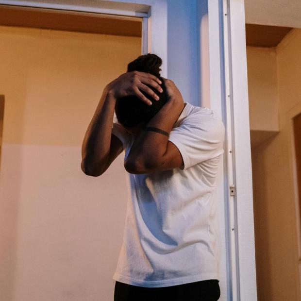 A person stands with head lowered, hands covering face.